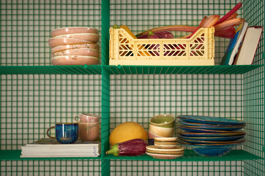 green open shelving pantry with ceramic deep plates, small plates and blue and pink coffee mugs
