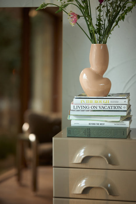 organic shaped flower vase in cream coral on a stack of books on top of a beige colored set of drawers
