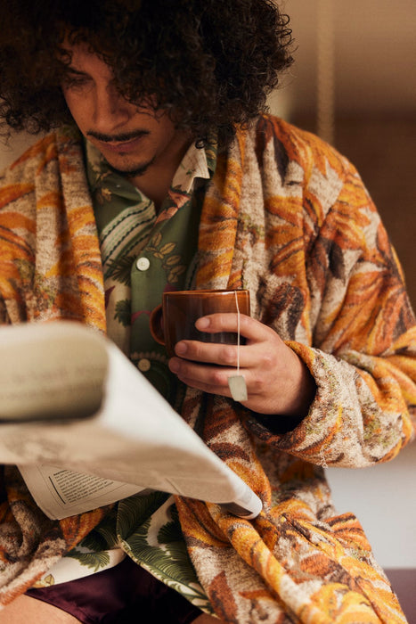 man reading newspaper wearing a bathrobe with pockets and orange brown palm tree motive