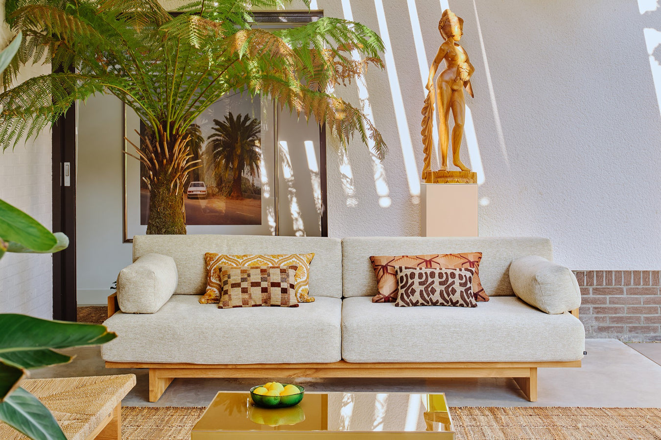 outdoor teak sofa with cream colored cushions, art work and palm tree