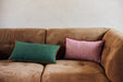 brown corduroy couch with a linen green lumbar pillow with orange trim and a pink linen pillow with red trim
