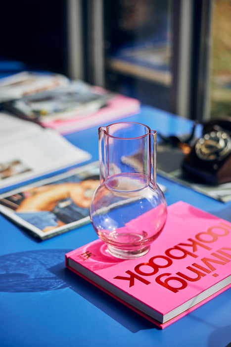small  pink glass vase  on a pink look book at a blue table