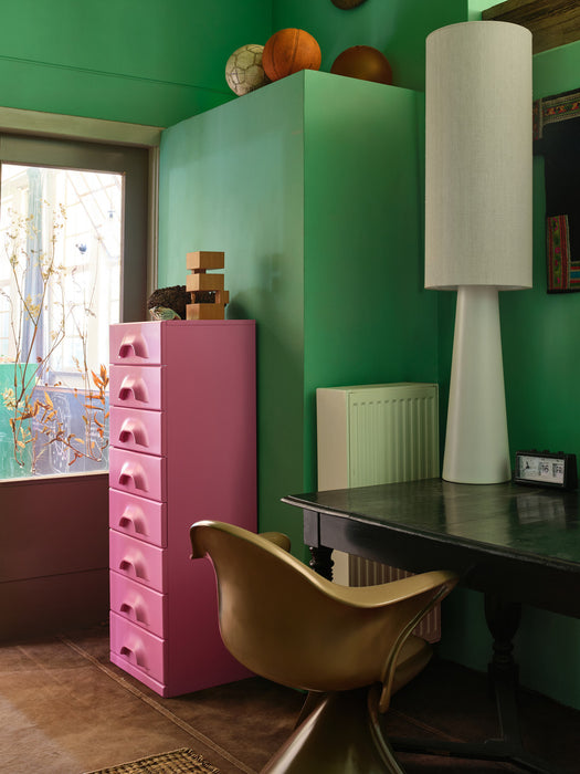 mahogany wooden sculpture with hand carved figurine in home office setting with pink drawers, green wall and large white cone table lamp