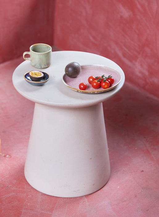 earthenware side table in a pink interior with plates and bowls on top of it