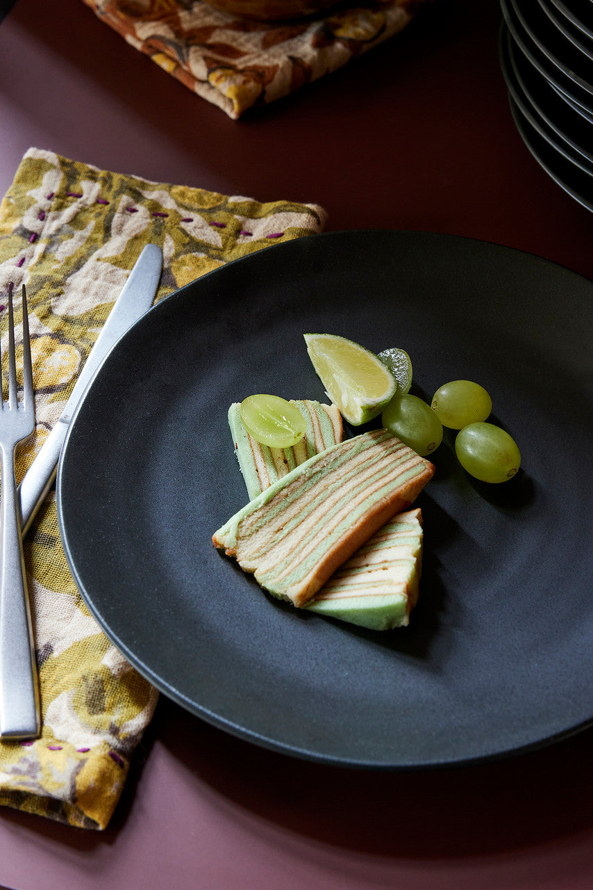 black dinner plate with cake and grapes and a retro style cotton napkin