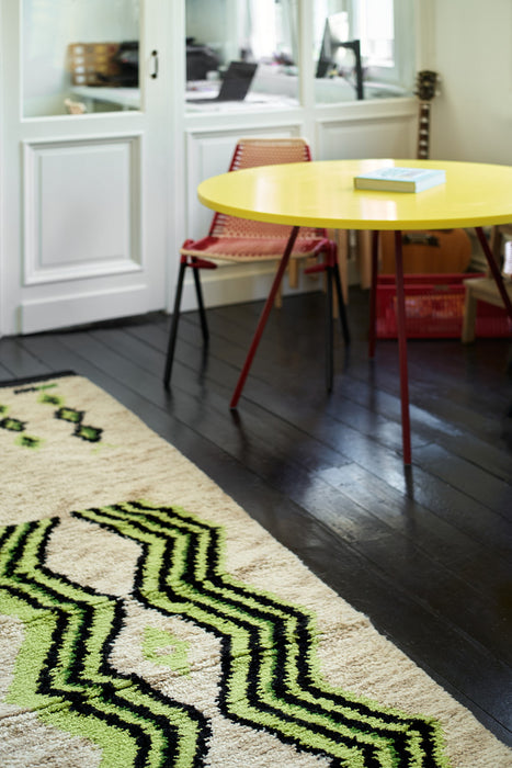 long runner made from hand knotted natural wool with neon green and black pattern next to a yellow round table and orange chair
