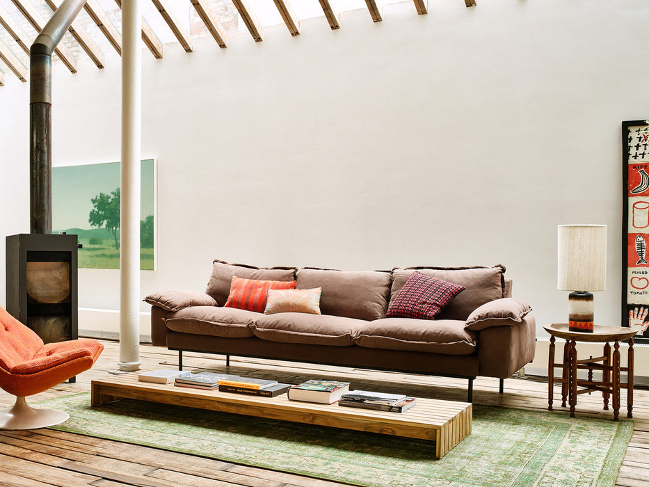 brown retro style sofa in a contemporary styled loft with low coffee table, orange chair and green painting