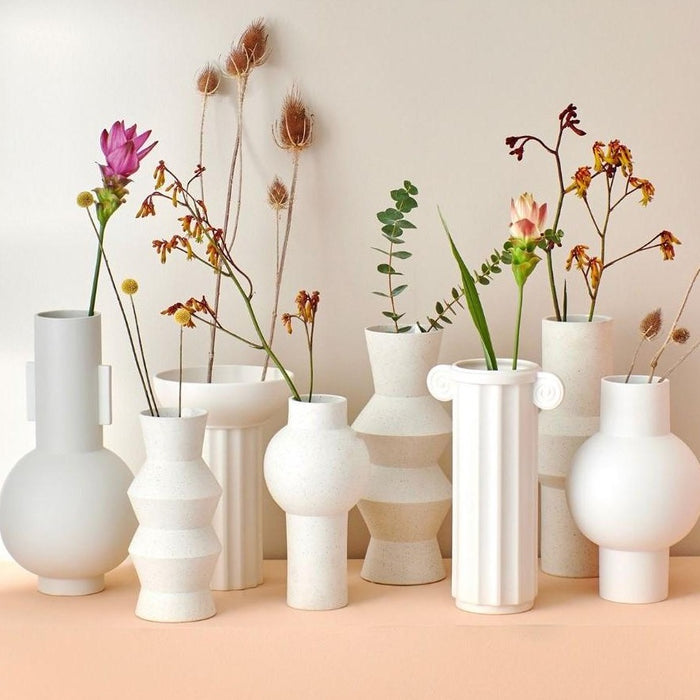 several white vases put together with single branches of flowers 