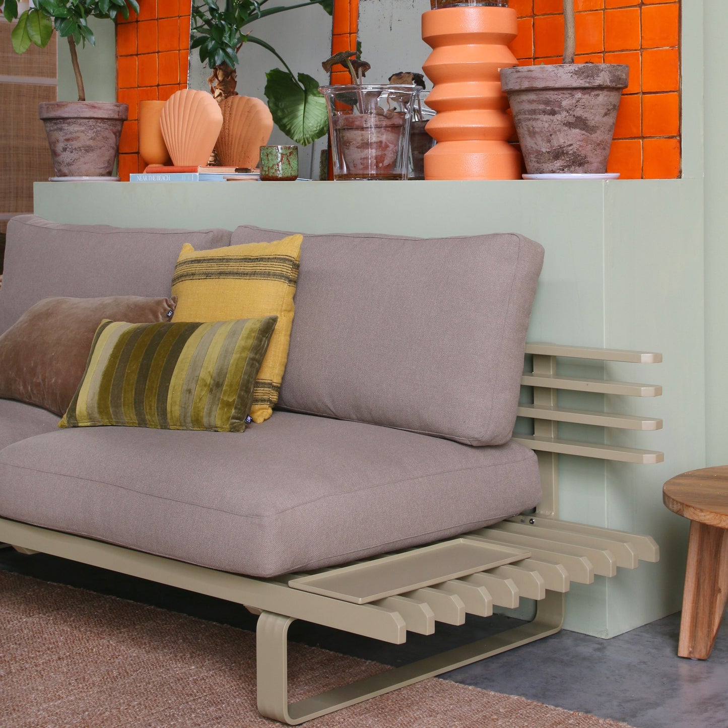 olive green aluminum sofa frame with brown seating against a green wall with orange accessories