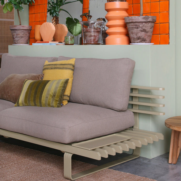 olive green aluminum sofa frame with brown seating against a green wall with orange accessories 