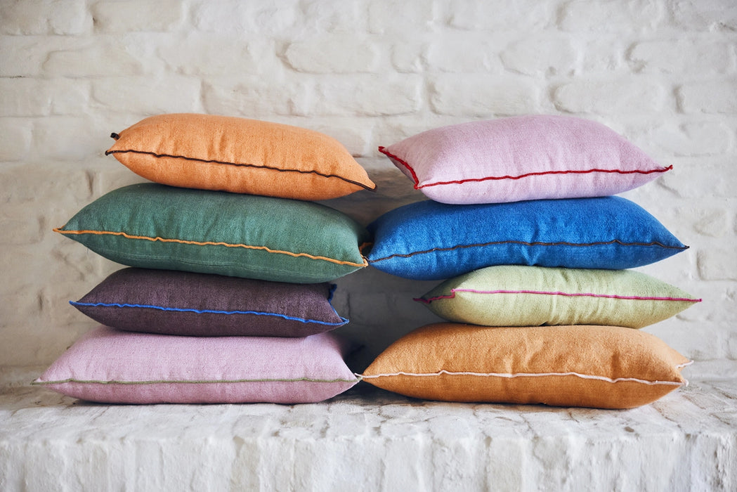 orange, green brown pink and blue colored lumbar shaped pillows with contrasting colors trim on two stacks