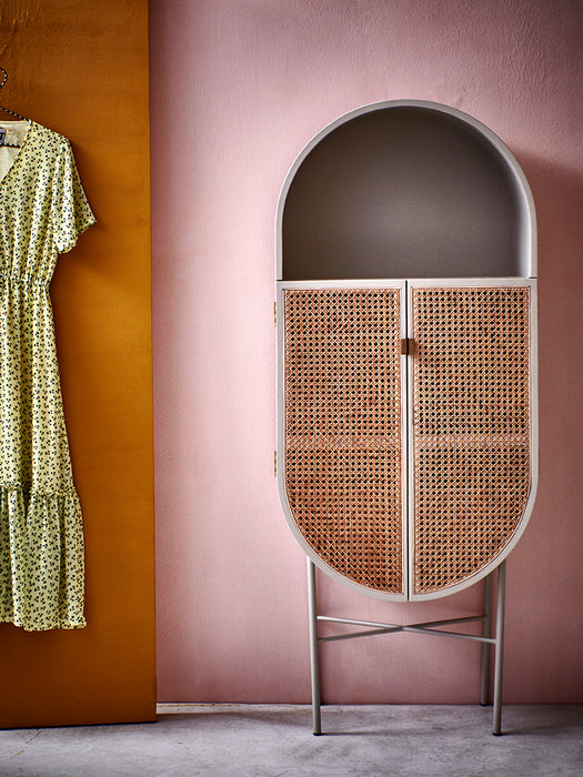 oval grey cabinet with cane webbing doors against a pink wall and a yellow dress