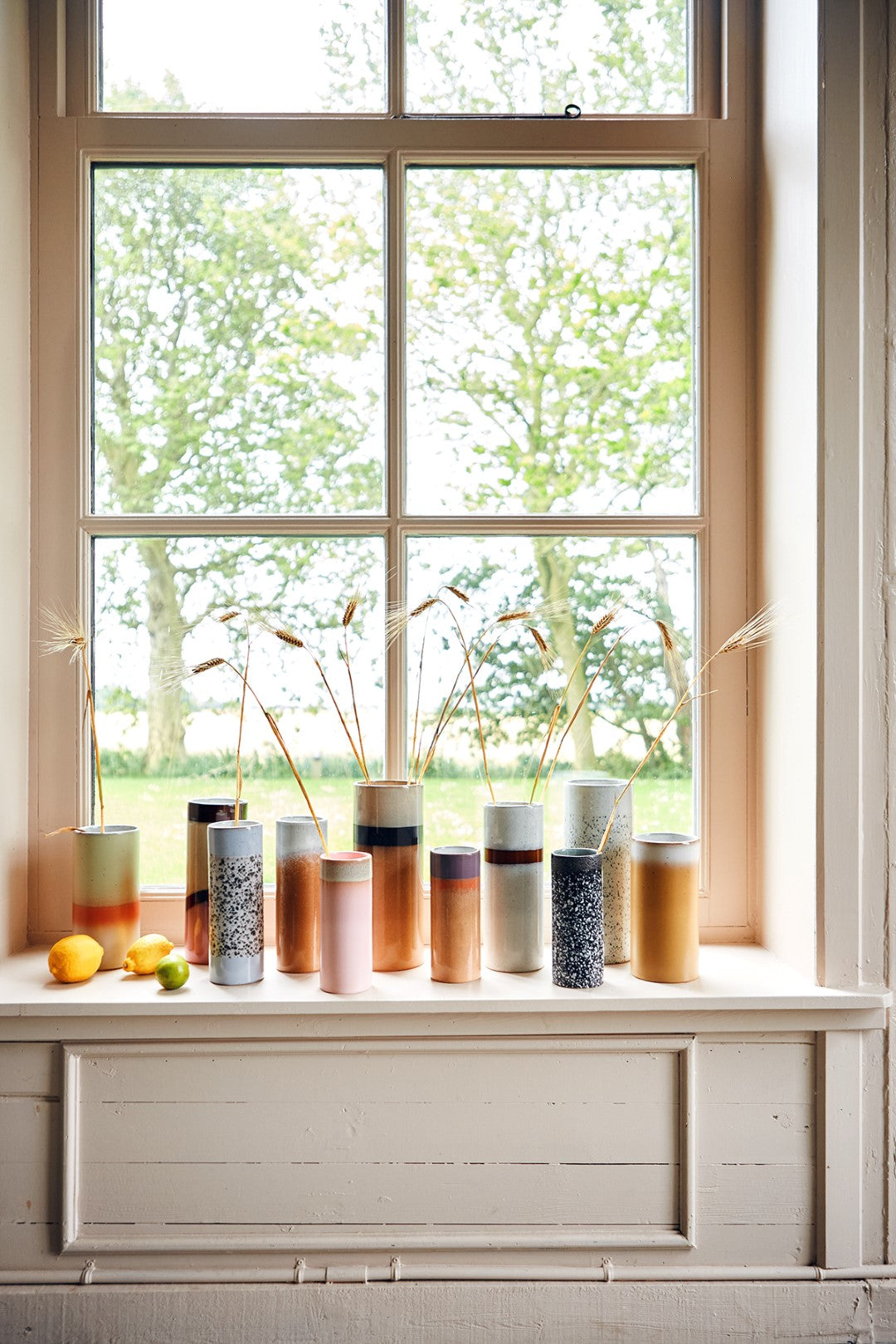 tall window with a group of stoneware retro style flower vases in various colors