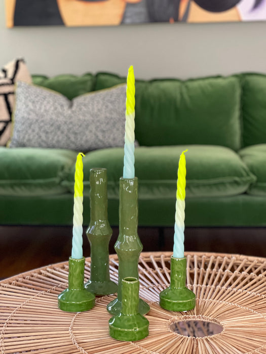 green ceramic candle stick holders with bright yellow and green and blue twisted candle on a wicker coffee table