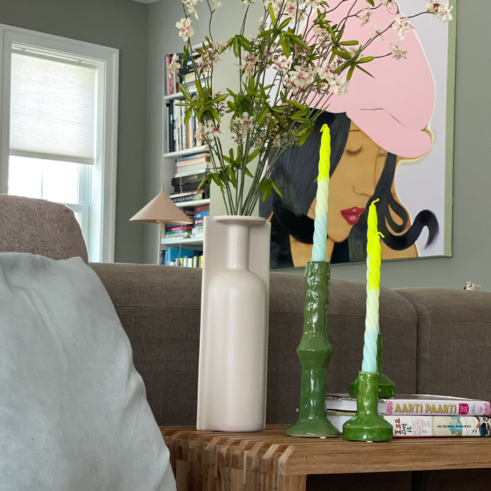 contemporary style interior with large painting of woman with pink head on the wall and two green candle stick holders with a candle on a teak slatted bench
