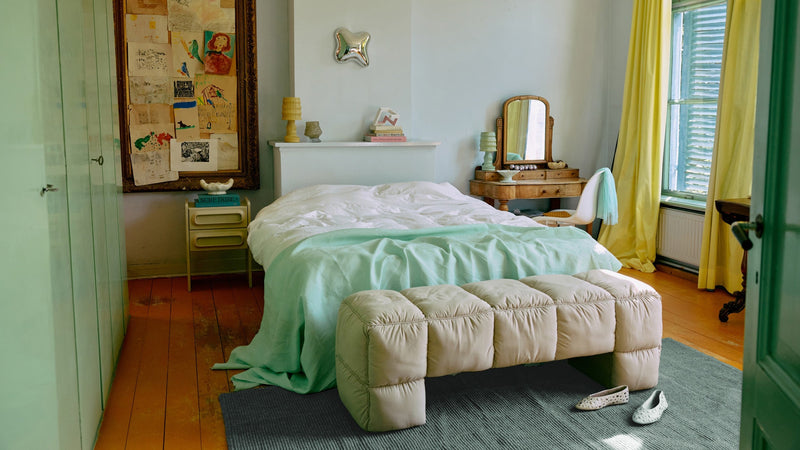 bedroom with green sheets, cream end of bed bench and green door