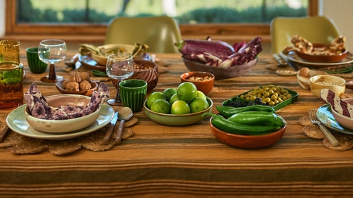 deep yellow plate with stoneware teaspoons in 4 colors and a white large basic dinner plate next to an orange bowl and a plate with green palm trees