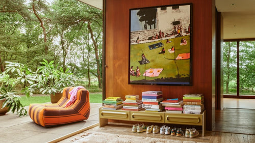 large painting of people in park over a lowboard stacked with books and sneakers