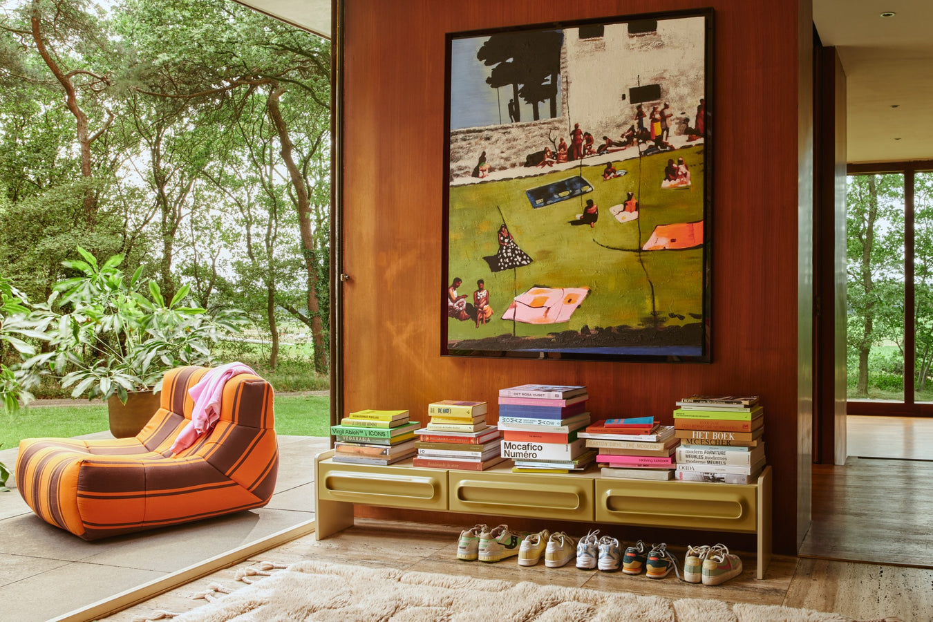 modern painting lowboard filled with stack of books and outdoor striped lounge chair