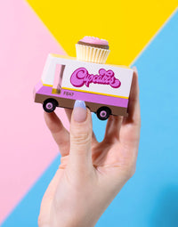 Hand holding a toy cupcake truck against a colorful background