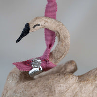 Decorative swan ornament with pink ribbon and silver tag on a stone surface