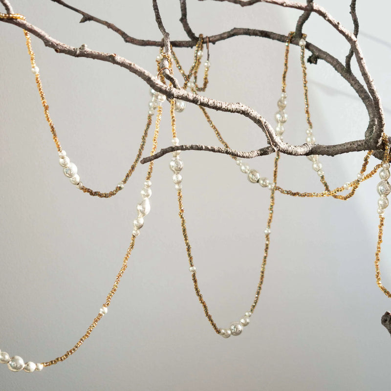 Garland with beads and amber brown chains hanging from a branch against a neutral background