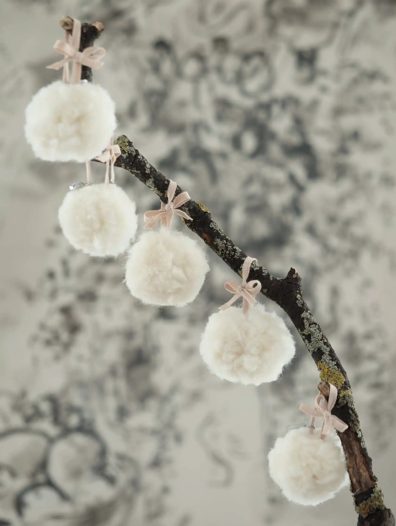 Decorative branch with white pom-poms and pink ribbons against a blurred background