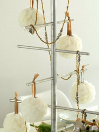 Decorative metal tree with white pom-pom ornaments and candles on a plain background