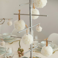 Decorative white pom-poms hanging from a metal tree on a table setting.