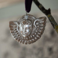 Silver angelic pendant with face design on a blurred background
