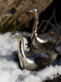 Metallic duck-shaped object in the snow with a blurred natural background