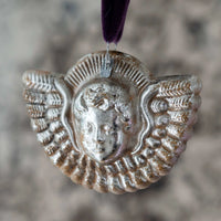 Decorative silver pendant with a face design on a blurred background