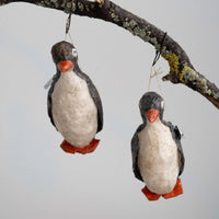 Two felted penguin ornaments hanging from a branch against a light background