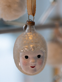 Decorative ornament with a face design inside a glass bulb, hanging against a blurred background.