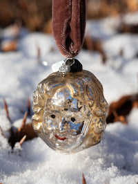 Decorative glass ornament with a face design hanging in the snow