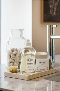 Bathroom counter with cleaning products and a glass jar on a wooden tray.