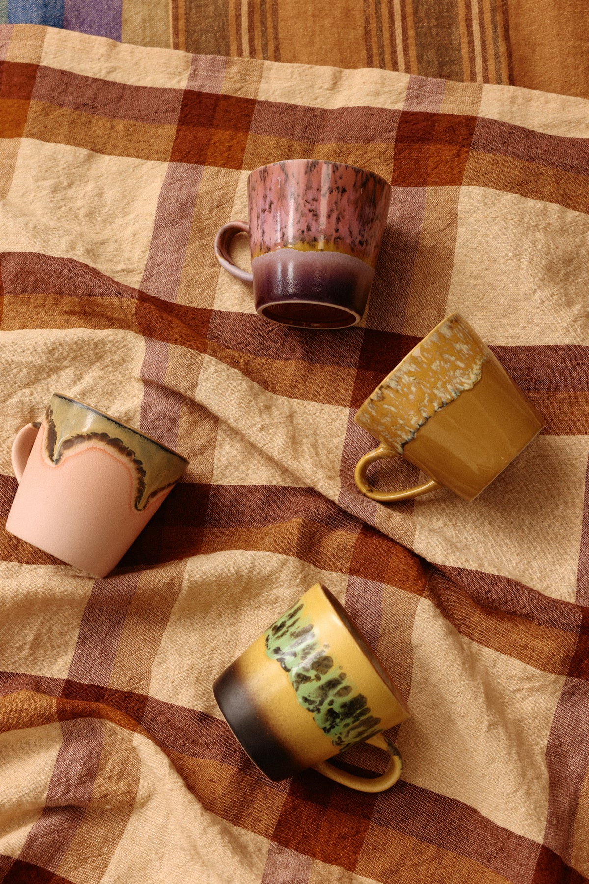 Four ceramic mugs on a checkered fabric background