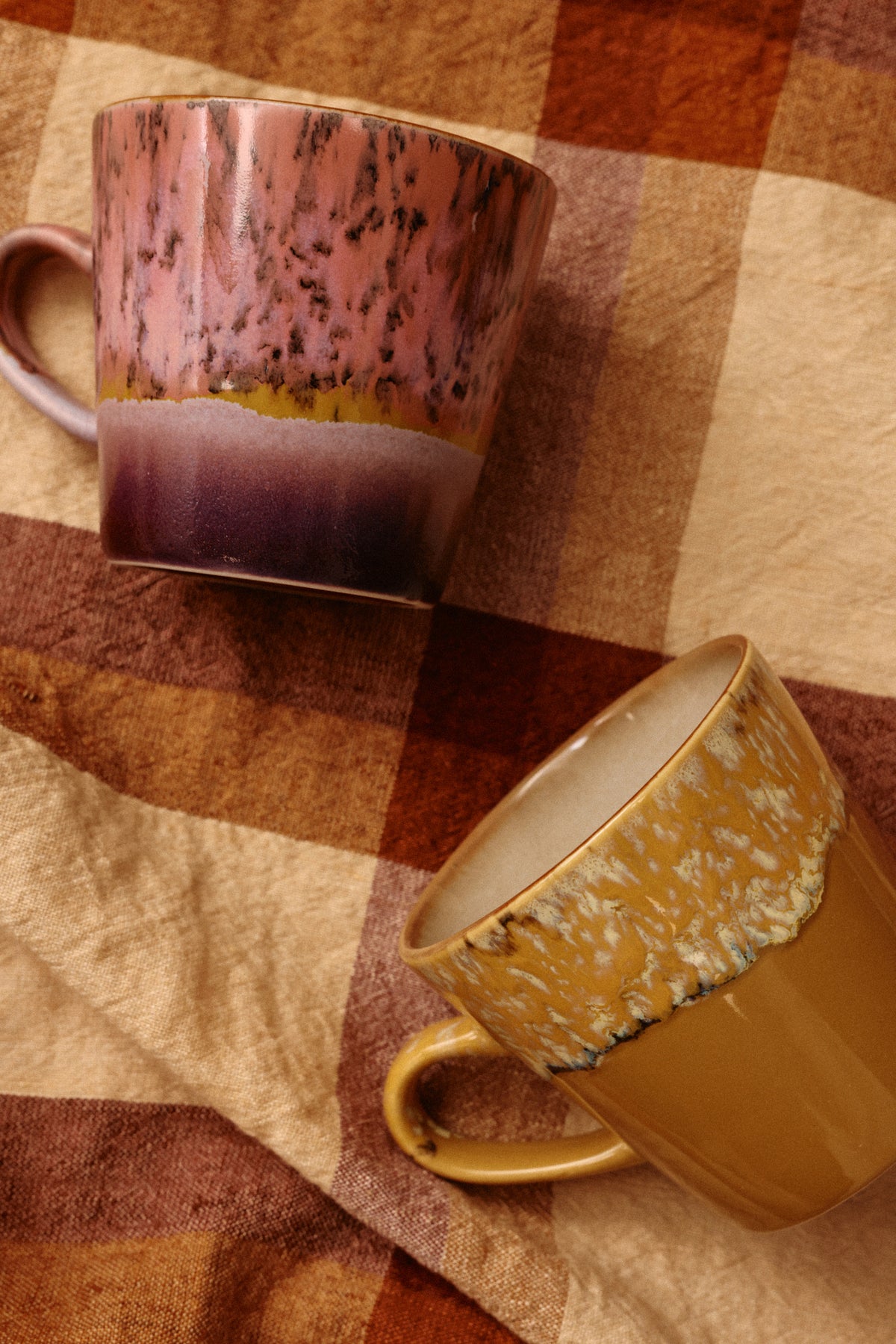 Two ceramic mugs with speckled glaze on a checkered fabric background