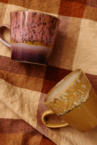 Two ceramic mugs with speckled glaze on a checkered fabric background