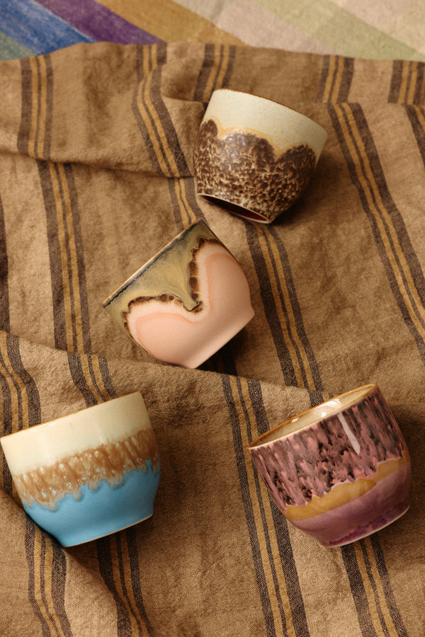 Set of ceramic cups with textured finishes on a striped fabric background