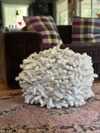 living room with pink woolen rug rugged textured off white pouf and brown velvet sofa