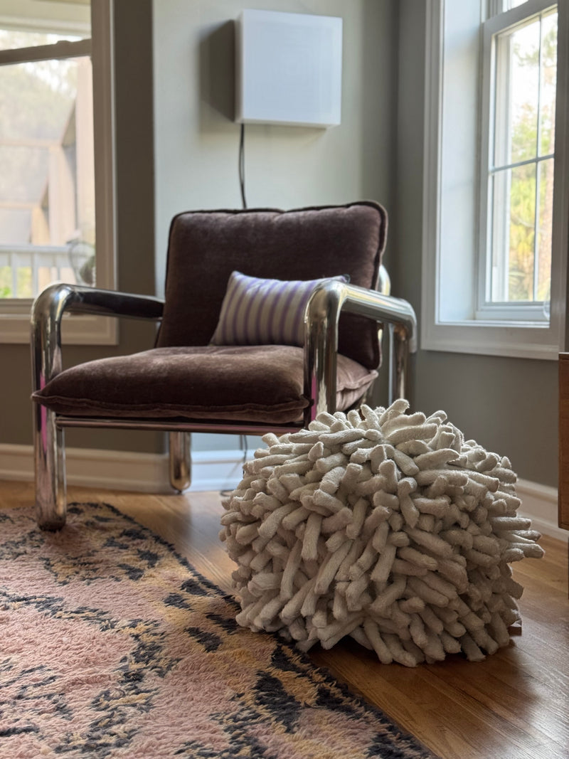 chrome and velvet lounge chair with off white textured pouf on wooden floor with pink wool rug