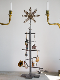 Decorative metal tree with hanging ornaments and candles on a plain background