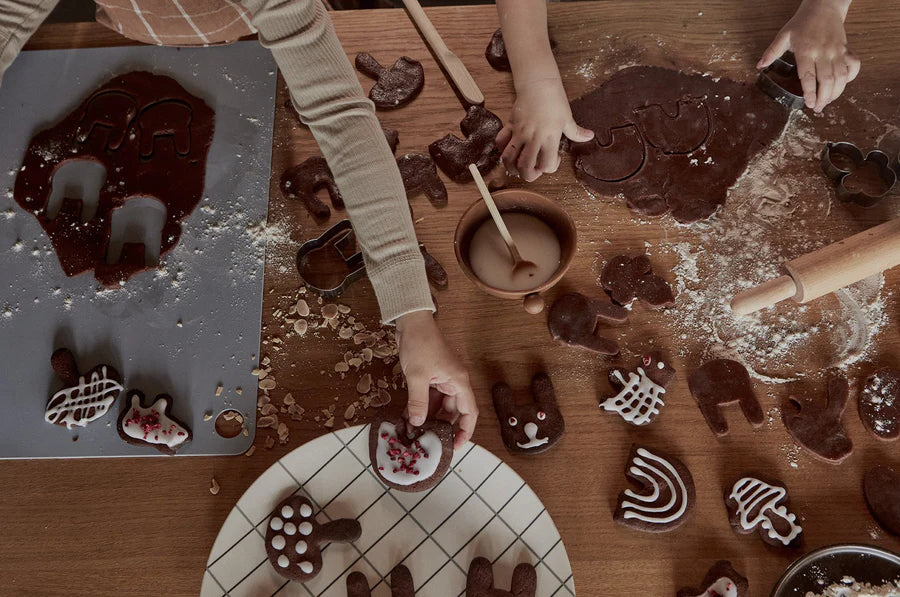 Children making chocolate cookies with molds on a wooden table.