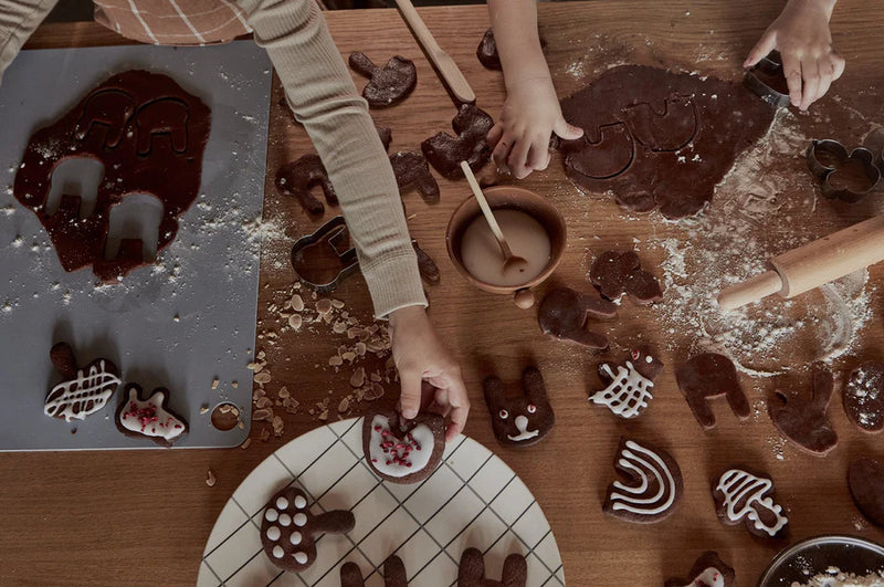 Children making chocolate cookies with molds on a wooden table.