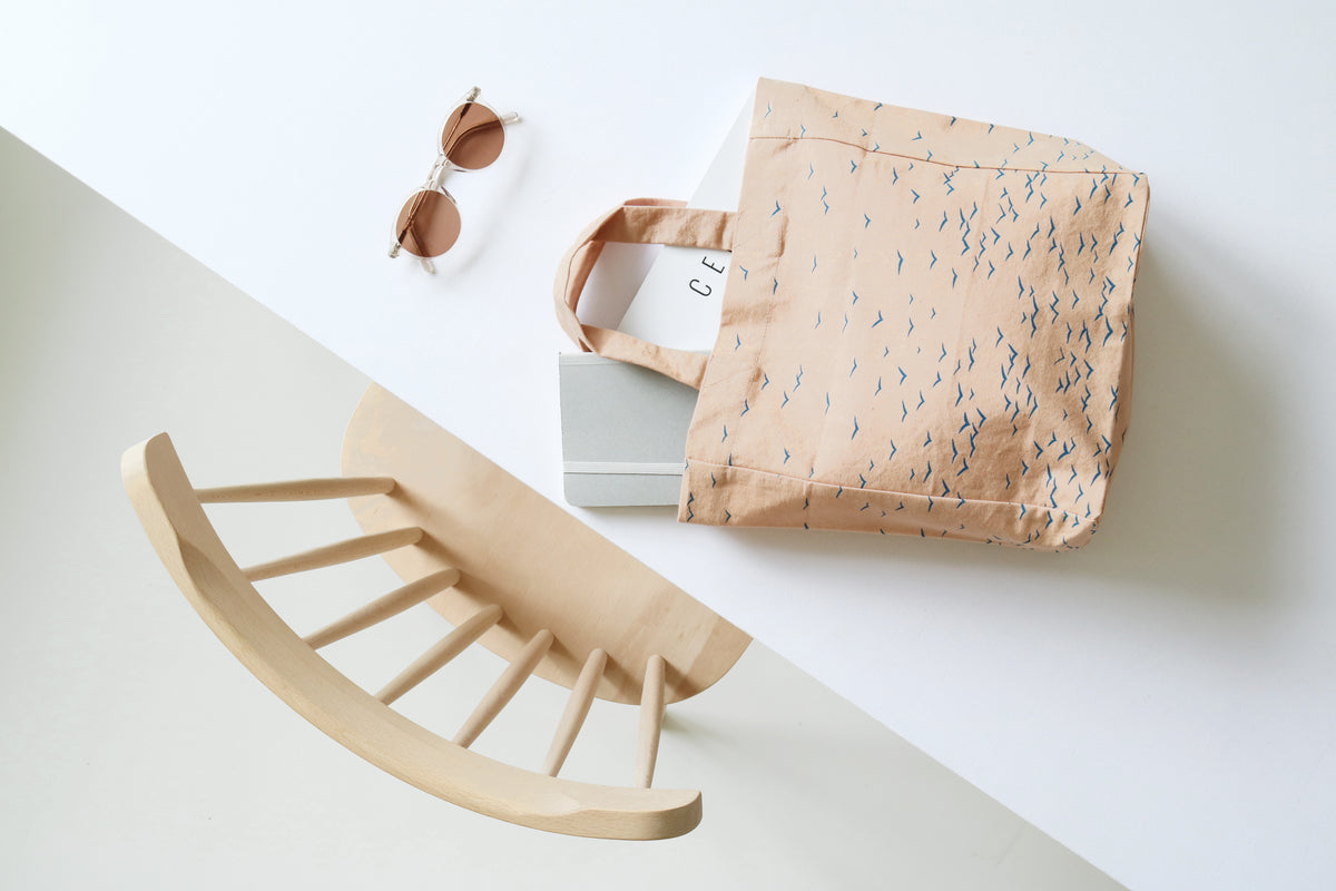 Beige baby rocker, sunglasses, and patterned bag on a light background