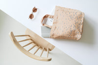 Beige baby rocker, sunglasses, and patterned bag on a light background