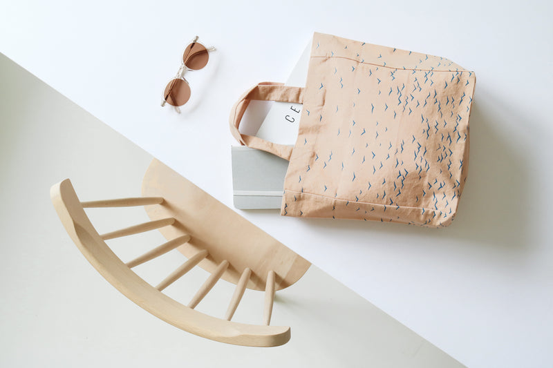 Beige baby rocker, sunglasses, and patterned bag on a light background