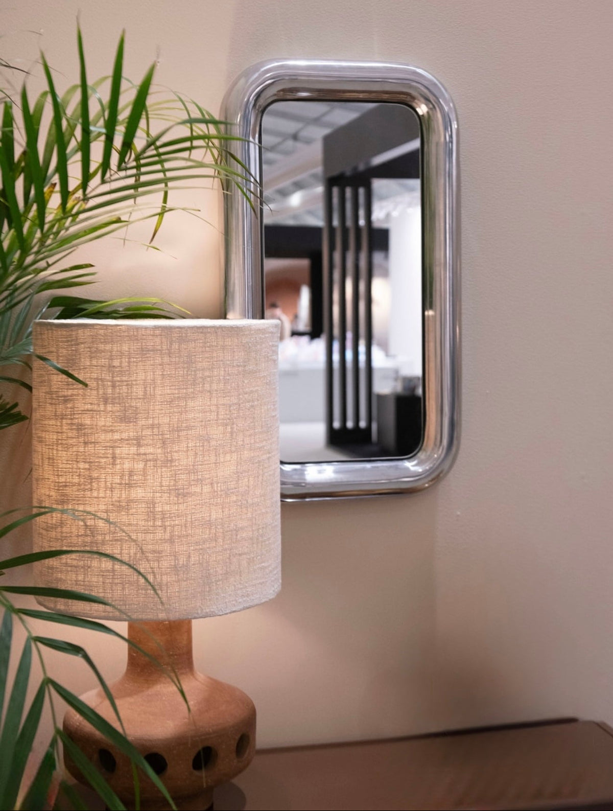 Decorative mirror with a lamp and plant on a table against a neutral wall.