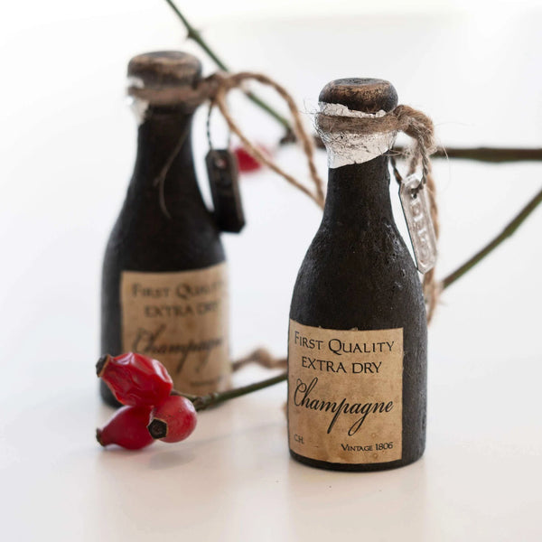 Two miniature champagne bottles with decorative labels on a white surface.